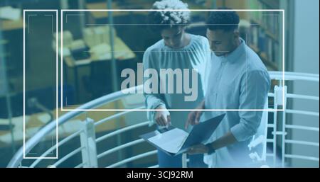 Collaborando con colleghi che visualizzano i dati sul computer portatile sul balcone dell'ufficio, con scaffali sottostanti Foto Stock