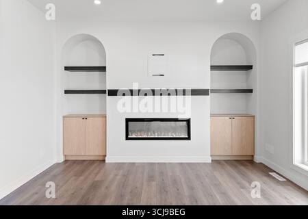 Al centro di una grande sala si trova un grande caminetto con un mantello nero. La camera è vuota e presenta una parete bianca e pavimenti in legno Foto Stock