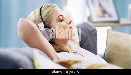 Occhi chiusi, cuffie e rilassati con la donna sul divano per un servizio di streaming, meditazione guidata e rumore bianco. Radio Zen, abbonamento e consapevolezza Foto Stock