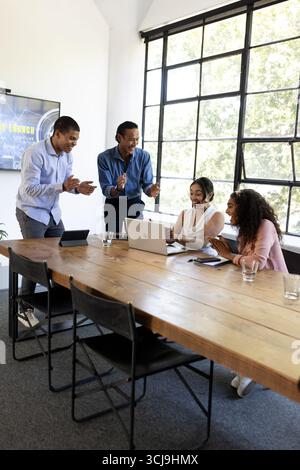 In ufficio, team diversificati che collaborano con notebook, condividendo con entusiasmo idee Foto Stock