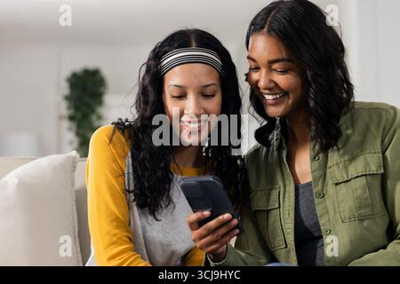 Madre e figlia sorridono mentre guardano lo smartphone insieme a casa Foto Stock