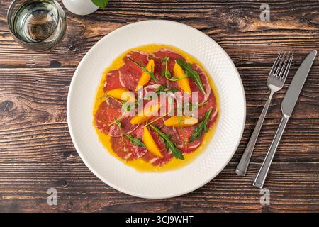 Carpaccio di manzo a fette sottili con segmenti di arancia e foglie di rucola Foto Stock