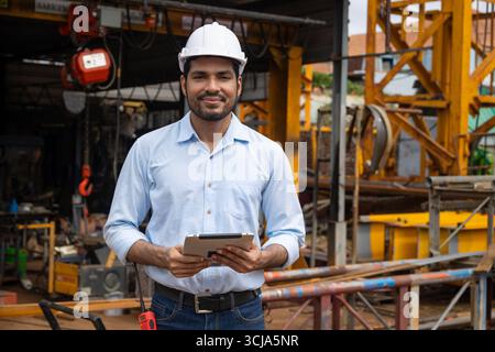 Ritratto ingegnere edile ispanico indiano lavoratore maschile nel cantiere con elmetto di sicurezza e tablet computer sorridente Foto Stock