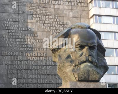 Busto in pietra di Karl Marx di fronte a un edificio con scritti comunisti multilingue, monumento di Karl Marx nel centro della città di Chemnitz, in Sassonia Foto Stock