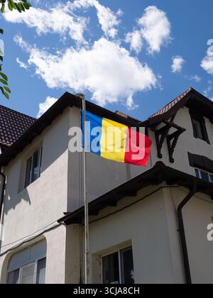 2025-08-24 Sinaia, Romania: Solo editoriale. Bandiera nazionale rumena che sventola sull'edificio con cielo blu e nuvole sullo sfondo. Foto Stock