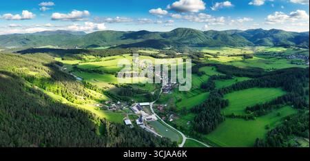 Tranquillo paesaggio con il villaggio rurale. verdi prati lussureggianti, case tradizionali e pittoresche montagne alpine sotto un blu chiaro sk Foto Stock