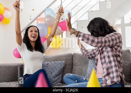 Festeggiando a casa, due donne si divertono con palloncini colorati e coriandoli Foto Stock