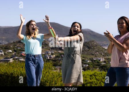 Donne che festeggiano all'aperto con coriandoli popper, esprimendo gioia ed eccitazione Foto Stock
