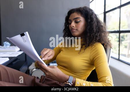 Donna d'affari sicura che esamina i documenti in un ufficio moderno, concentrandosi sui dettagli Foto Stock