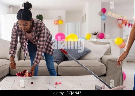 Ripulisce dopo la festa, la donna rimette in ordine il soggiorno con palloncini e coriandoli Foto Stock