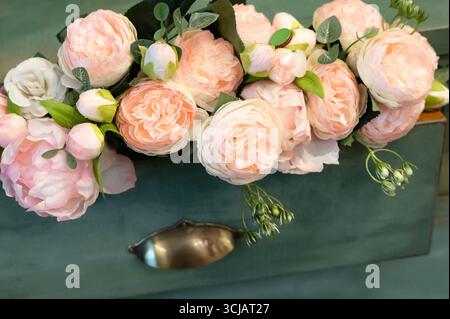 Una splendida disposizione floreale caratterizzata da rose rosa tenui e da una vegetazione delicata collocata elegantemente su uno sfondo color verde acqua, perfetta per l'arredamento della casa o per eventi Foto Stock
