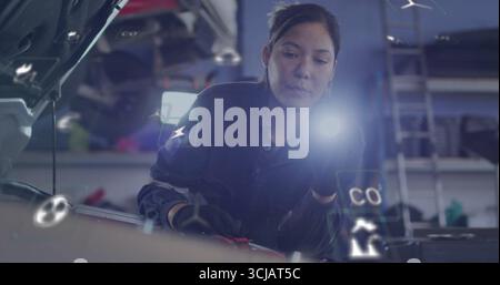 Ispezionare il tecnico indossando tute controllare il motore sotto il cofano in garage con icone diagnostiche Foto Stock