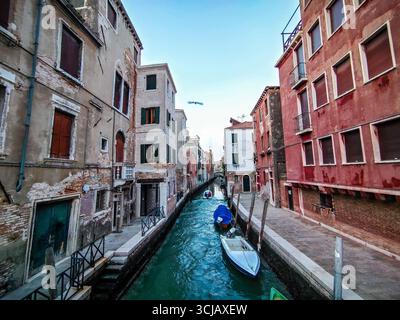 Una mattinata tranquilla su un pittoresco canale di Venezia, in Italia. L'immagine cattura le acque turchesi brillanti che riflettono le facciate logore di un edificio storico Foto Stock