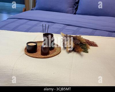 Letto con biancheria blu e set decorativo di candele, diffusore e fiori secchi. Comfort, stile di vita e atmosfera accogliente in un design moderno. Foto Stock
