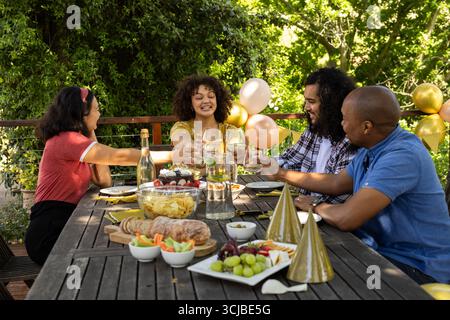 Brindate con bicchieri da vino, amici che festeggiano e condividono i pasti festivi all'aperto Foto Stock