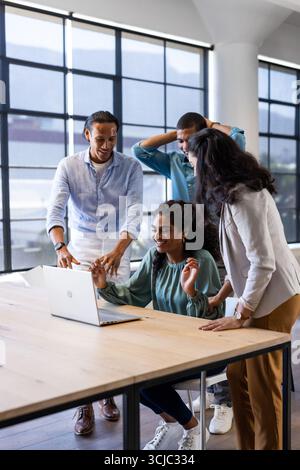 Festeggiamo il successo, un team aziendale diversificato che collabora con un notebook in un ufficio moderno Foto Stock