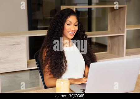 Una donna latina sicura di sé con i capelli ricci lavora sul suo laptop in un moderno ufficio di coworking. Si concentra intensamente, incarnando professionalità ed efficienza Foto Stock