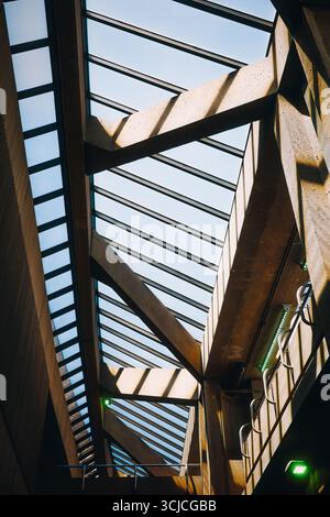 Basso angolo di suggestiva veduta della moderna architettura aeroportuale caratterizzata da lucernari geometrici e strutture in metallo. La luce solare filtra, evidenziando t Foto Stock
