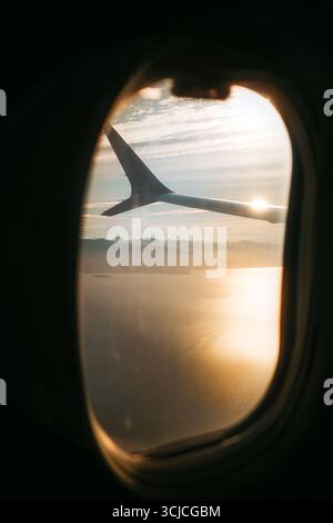 Una splendida vista dalla finestra di un aereo che mostra l'ala sullo sfondo di un tranquillo tramonto, catturando la tranquilla bellezza di volare sopra le nuvole Foto Stock