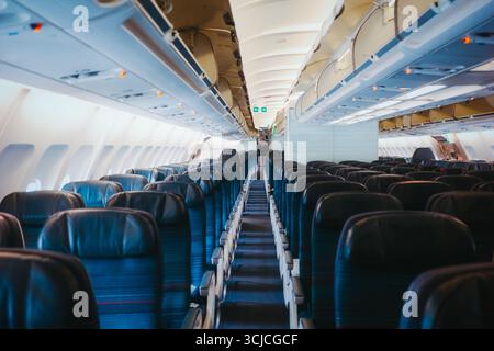Una spaziosa cabina dell'aereo che mostra file di sedili vuoti e blu e vani a padiglione. La luce naturale scorre attraverso le finestre, offrendo un ambiente pulito e pulito Foto Stock