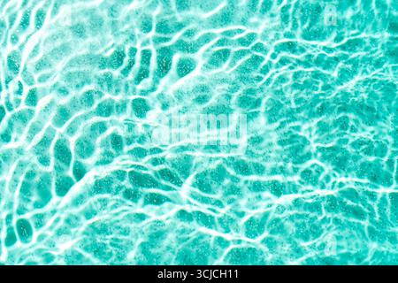 La superficie dell'acqua turchese chiara mostra intricati motivi di onde ondulate e riflessi luminosi scintillanti. La trama aggiunge profondità e movimento, cre Foto Stock