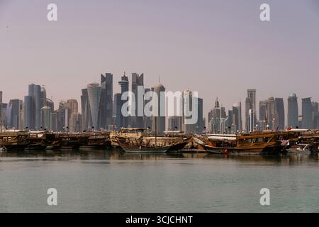 Tradizionali dhow in legno ancorati vicino al bordo dell'acqua con il moderno skyline di Doha, Qatar, che si innalzano dietro di loro. Questa scena contrasta splendidamente Foto Stock