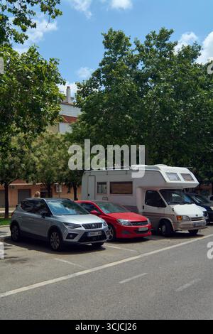 Viladecans. Barcellona - 06 settembre 2025: Una linea di veicoli parcheggiati, tra cui un camper, un'auto rossa e un SUV grigio, su una strada soleggiata Foto Stock