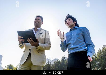 Due partner aziendali si impegnano in una discussione all'aperto a Melbourne, utilizzando un tablet per la pianificazione e la strategia. La scena riflette il lavoro di squadra, l'innovazione, Foto Stock