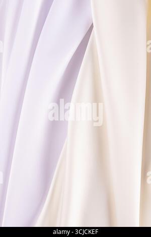 Un lussuoso tessuto satinato in morbide tonalità di bianco e crema, delicatamente piegato per creare uno sfondo elegante e liscio. Ideale per matrimoni, eventi o io Foto Stock