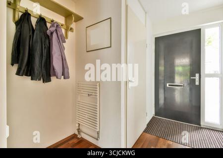 Un ingresso moderno caratterizzato da un'elegante porta nera, appendiabiti minimalisti per giacche e caldo pavimento in legno, creando un bancomat invitante e funzionale Foto Stock