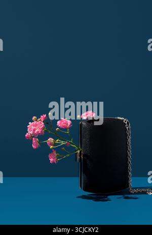 Elegante esposizione di fiori rosa naturali collocati con grazia all'interno di un'elegante borsa nera su un vivace sfondo blu. Perfetto per un ambiente moderno e minimale Foto Stock
