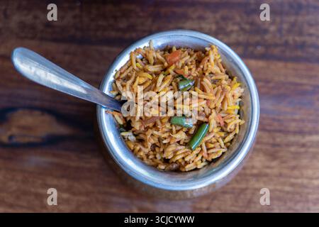Biryani allo zafferano Navratico con verdure fresche, spezie e riso basmati in una pentola di metallo su sfondo di legno, vista ravvicinata dall'alto. Cucina indiana Foto Stock