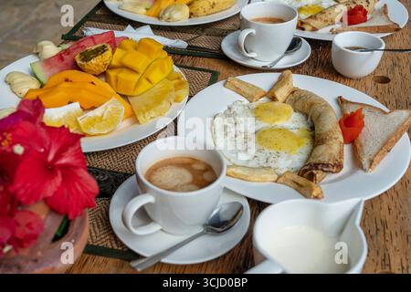 Colazione tropicale a base di frutta, caffè e uova strapazzate e pancake alla banana per due sulla spiaggia vicino al mare nel ristorante dell'hotel, isola di Zanzibar, Tanzania Foto Stock