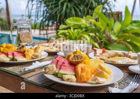 Colazione tropicale a base di frutta, caffè e uova strapazzate e pancake alla banana per due sulla spiaggia vicino al mare nel ristorante dell'hotel, isola di Zanzibar, Tanzania Foto Stock