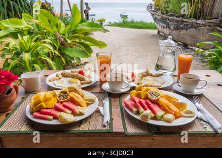 Colazione tropicale a base di frutta, caffè e uova strapazzate e pancake alla banana per due sulla spiaggia vicino al mare nel ristorante dell'hotel, isola di Zanzibar, Tanzania Foto Stock
