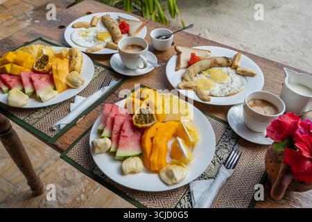 Colazione tropicale a base di frutta, caffè e uova strapazzate e pancake alla banana per due sulla spiaggia vicino al mare nel ristorante dell'hotel, isola di Zanzibar, Tanzania Foto Stock