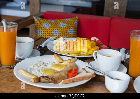 Colazione tropicale a base di frutta, caffè e uova strapazzate e pancake alla banana per due sulla spiaggia vicino al mare nel ristorante dell'hotel, isola di Zanzibar, Tanzania Foto Stock
