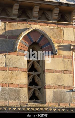 Un primo piano di una finestra in stile gotico con intricati tracciati, adagiato all'interno di un muro di pietra e mattoni. La luce del sole mette in risalto l'architettura dettagliata Foto Stock