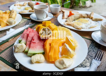 Colazione tropicale a base di frutta, caffè e uova strapazzate e pancake alla banana per due sulla spiaggia vicino al mare nel ristorante dell'hotel, isola di Zanzibar, Tanzania Foto Stock