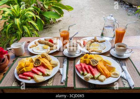 Colazione tropicale a base di frutta, caffè e uova strapazzate e pancake alla banana per due sulla spiaggia vicino al mare nel ristorante dell'hotel, isola di Zanzibar, Tanzania Foto Stock