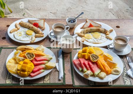 Colazione tropicale a base di frutta, caffè e uova strapazzate e pancake alla banana per due sulla spiaggia vicino al mare nel ristorante dell'hotel, isola di Zanzibar, Tanzania Foto Stock