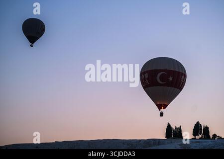 pamukkale, Turkiye, 08.07.2025 mongolfiera con bandiera turca che sventola al tramonto sulle terrazze in travertino di pamukkale. Viaggio avventura e pamukkale c Foto Stock