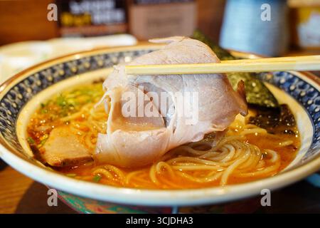 Ramen giapponese con grande maiale Chashu sollevato dai bastoncini di cioccolato Foto Stock