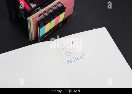 quaderno scritto sul ritorno a scuola con le scorte scolastiche dietro Foto Stock
