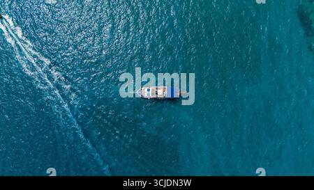 Zante, Grecia, vista aerea di una singola barca che galleggia nel turchese Mar Ionio con acque ondulate calme e linee bianche sulla superficie dell'oceano Foto Stock