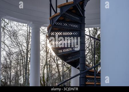 Scala a chiocciola in metallo con gradini in legno, posizionata tra colonne e alberi, creando una prospettiva unica e un'atmosfera invitante per l'alto Foto Stock
