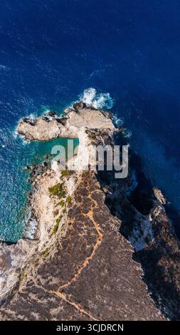 Vista dall'alto della spiaggia di Plakaki, la penisola rocciosa di Zante, Grecia, incontra fondali turchesi e blu scuro del Mar Ionio con ripide scogliere aride nell'entroterra Foto Stock