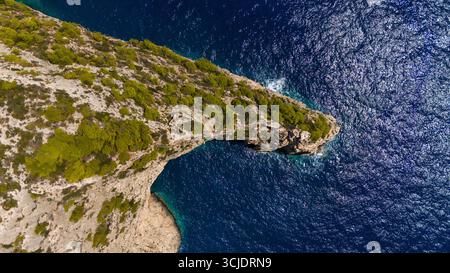 Zante Grecia vista aerea della scogliera costiera rocciosa coperta da pini verdi che si estendono nel profondo blu del Mar Ionio con onde scintillanti alla luce del sole Foto Stock