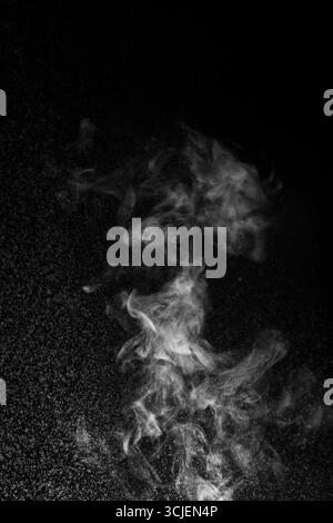 Il fumo bianco o il vapore sottile ruotano verso l'alto su uno sfondo nero in uno stile astratto drammatico, evocando mistero, movimento e atmosfera Foto Stock