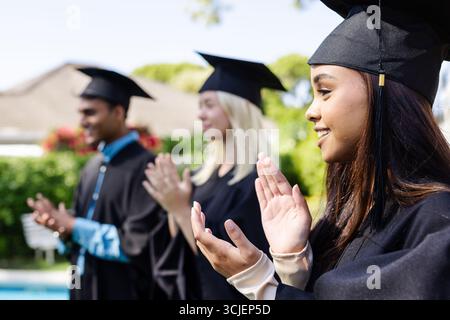 Laureati in berretti e camici che battono all'aperto, celebrando i risultati accademici Foto Stock